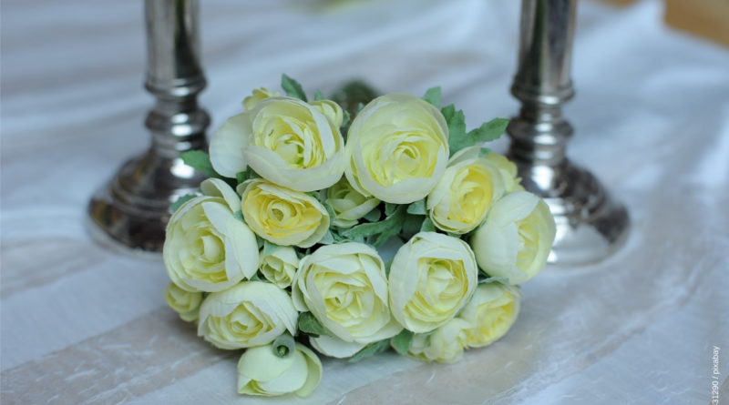 Weiße Rosen aus weißer Tischdecke mit zwei silbernen Kerzenständern.